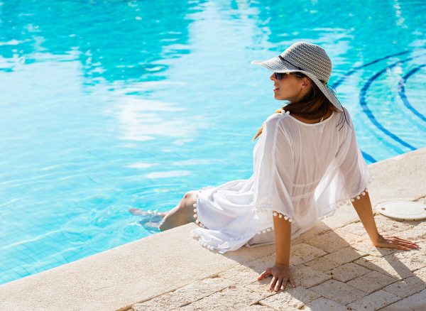 Base Tans & Other Myths About Tanning, Sunburns, & Skin Cancer Woman relaxing poolside in hat & coverup