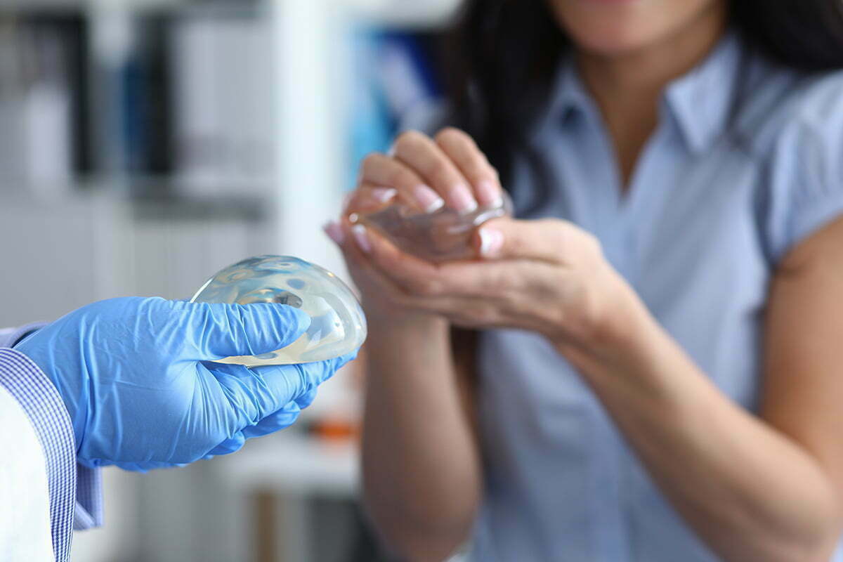 breast augmentation patient holds clear breast implant in hands while consulting with plastic surgeon