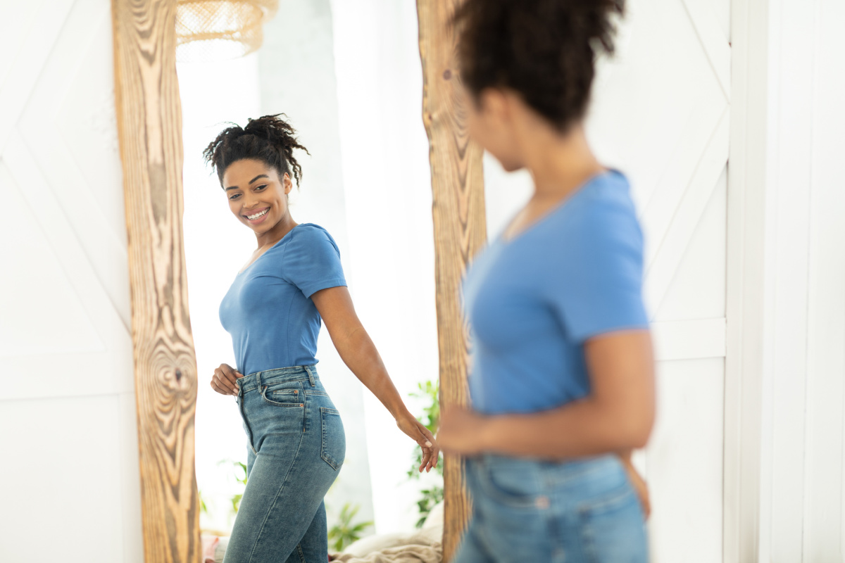 Woman smiles in mirror after procedures to reduce tummy pooch