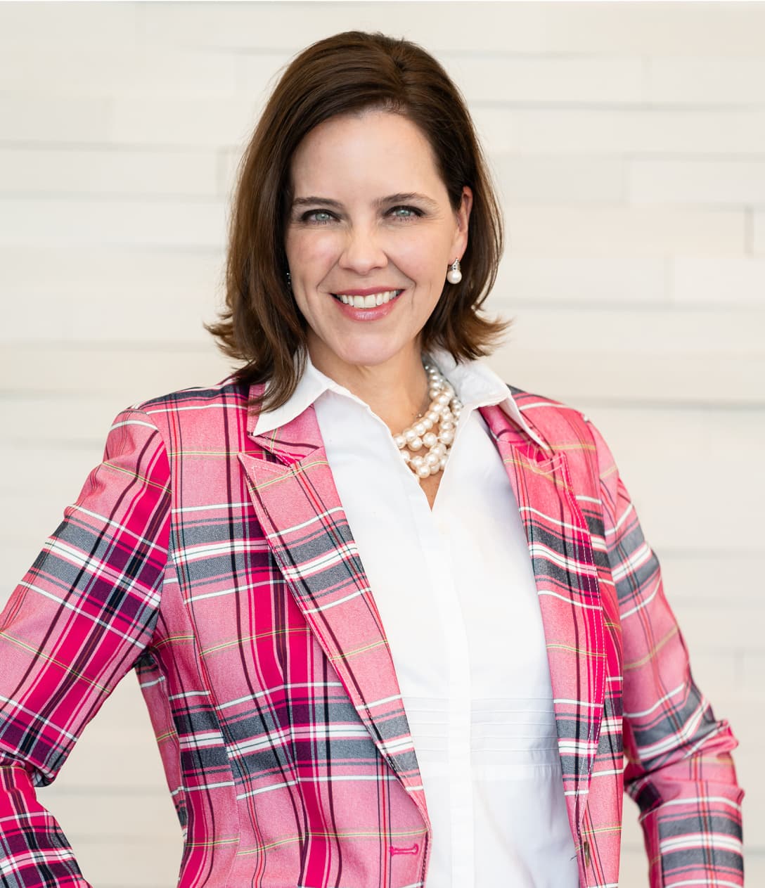 Dr. Kirby stands smiling wearing a plaid pink blazer standing outside the state-of-the-art plastic surgery center located at Kirby Plastic Surgery in Fort Worth.