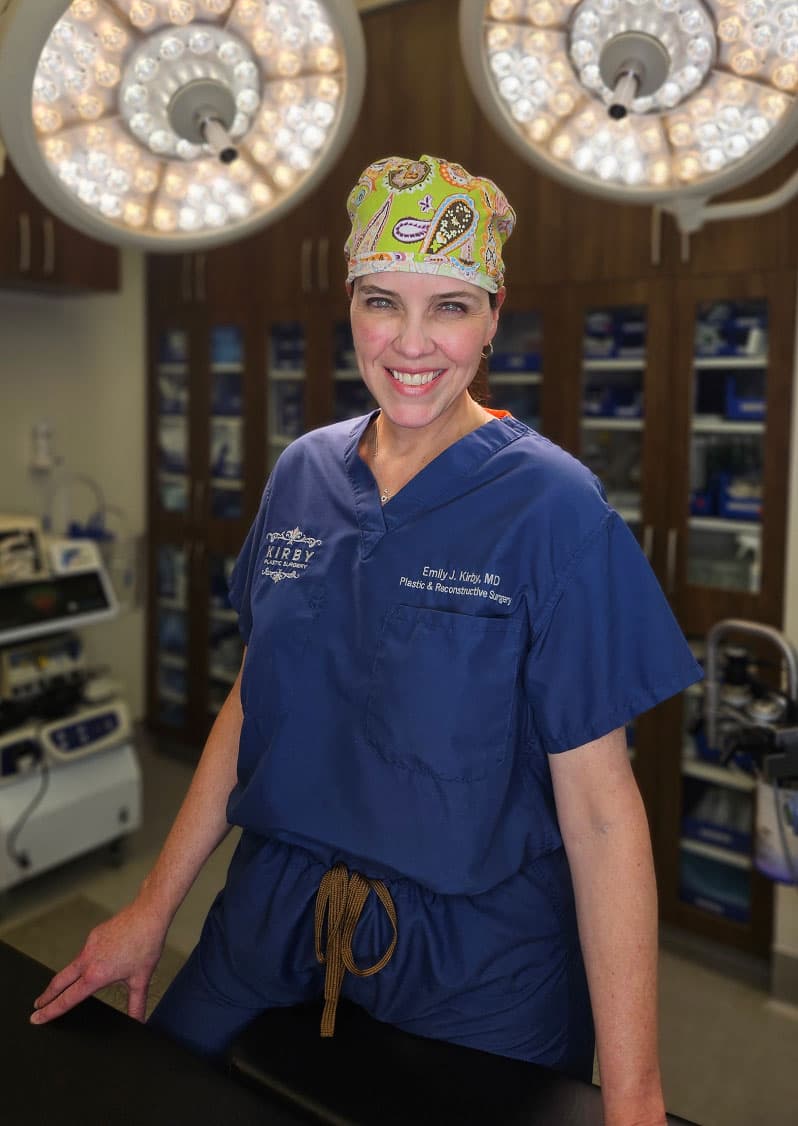 Portrait of Female Board Certified Plastic Surgery Emily J. Kirby, MD, in operating room wearing scrubs, smiling