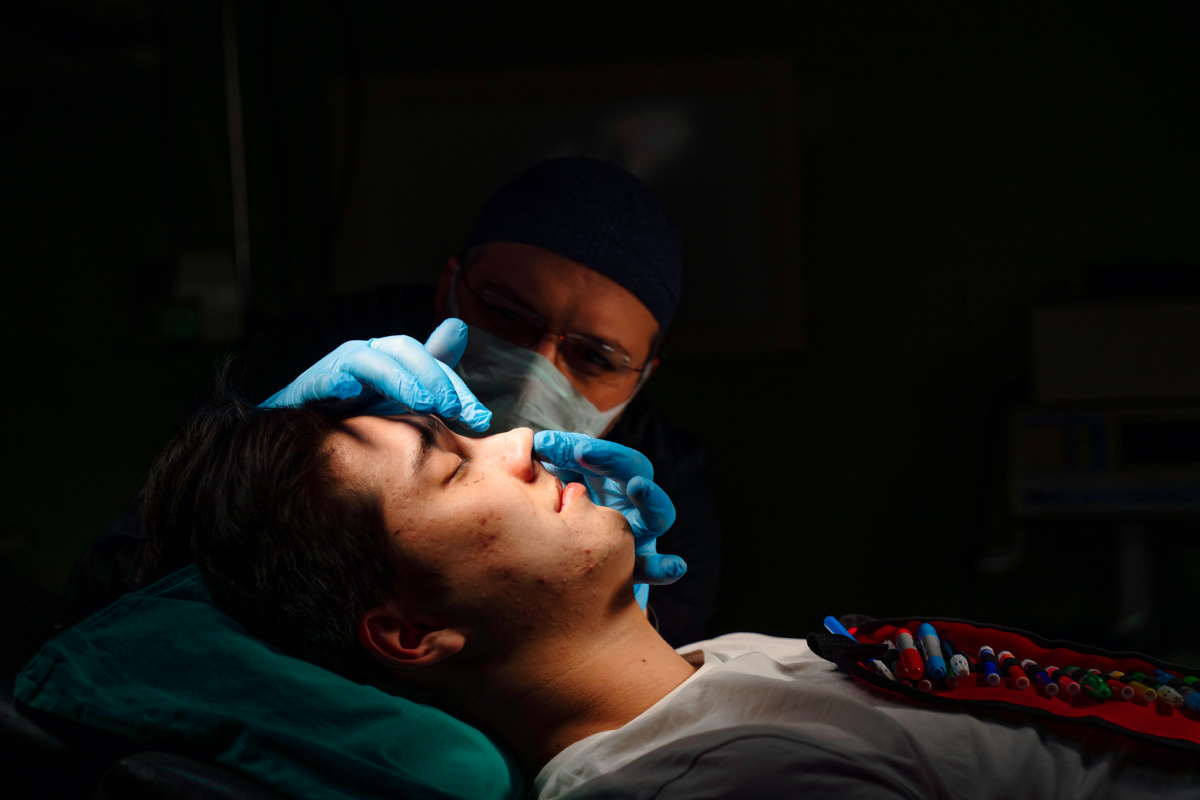 Plastic surgeon performing rhinoplasty in dark operating room