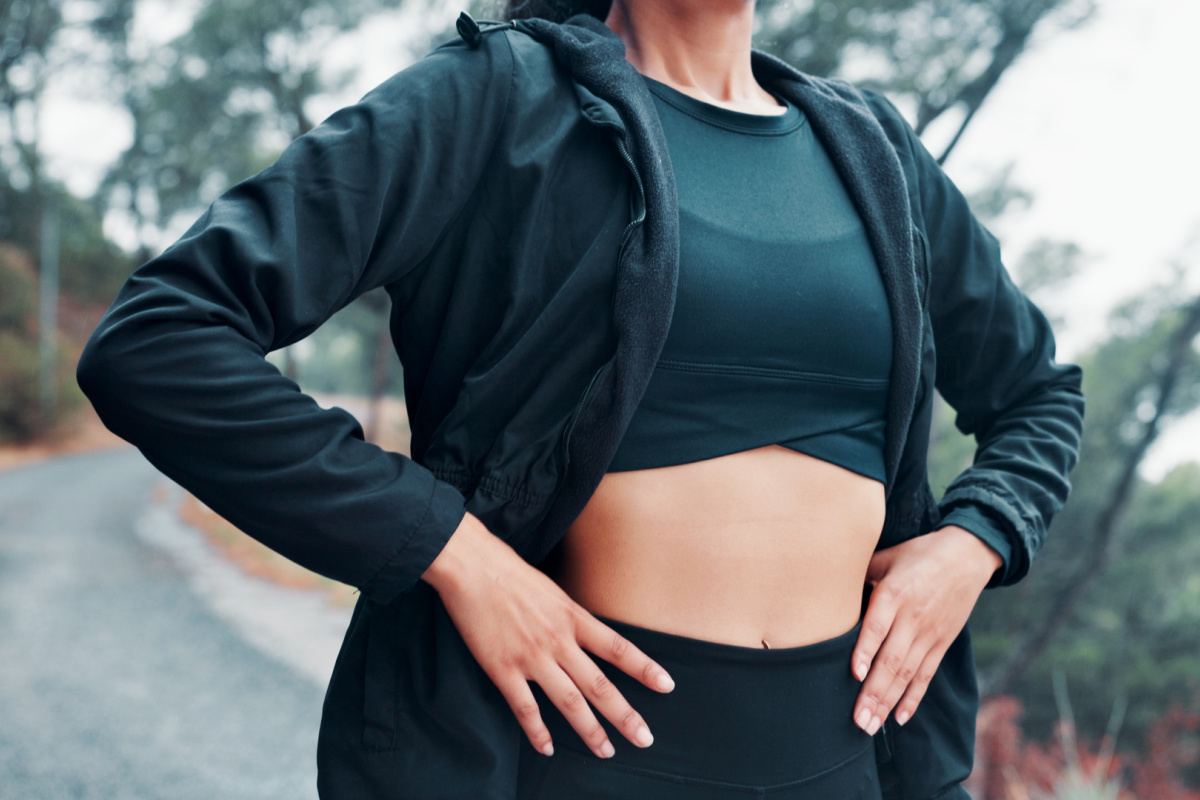 Faceless woman in workout gear with fit abdomen after post-weight loss tummy tuck and liposuction